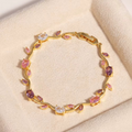 Close-up of the gold floral bracelet showing pink and purple gemstones on beige background