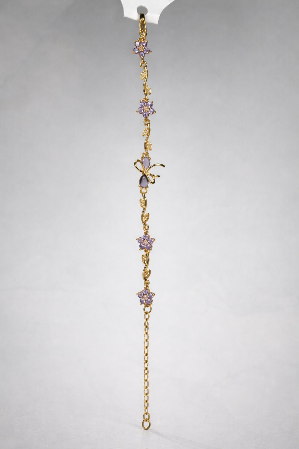 Gold bracelet with purple amethyst flowers and butterfly charm hanging vertically