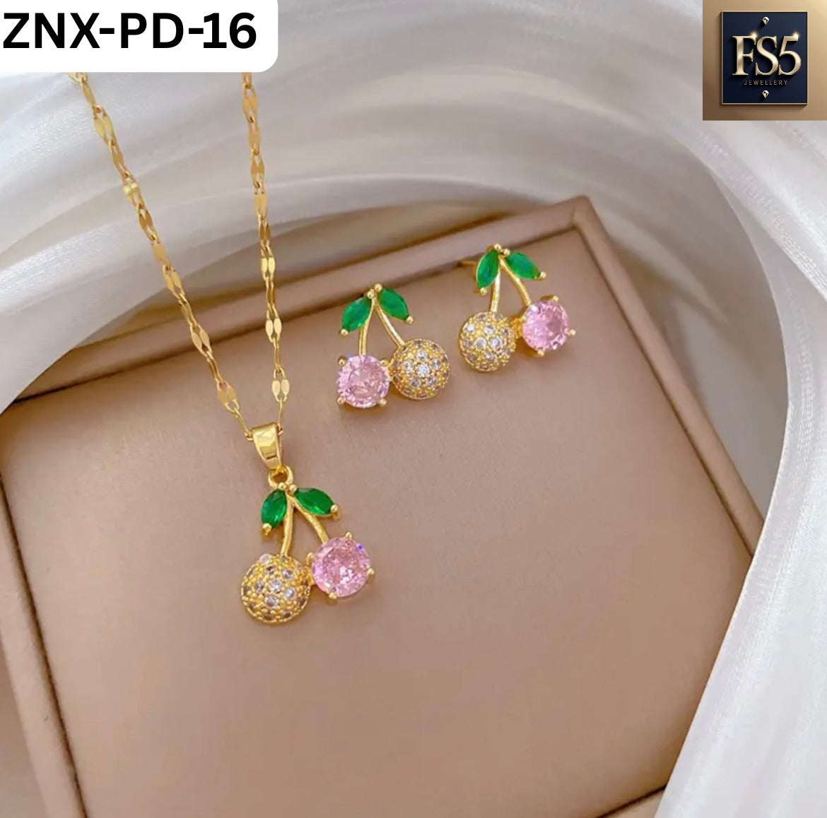 Gold-tone cherry pendant necklace and matching earrings with pink and clear crystals and green leaf accents on beige background