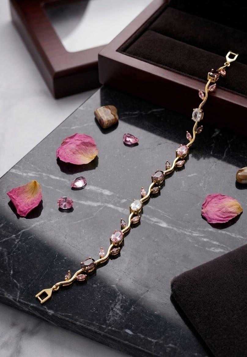 Gold-tone bracelet with pink and clear gemstones laid on black marble surface with rose petals