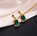 Pair of gold earrings featuring large faceted green rectangular stones surrounded by clear crystals