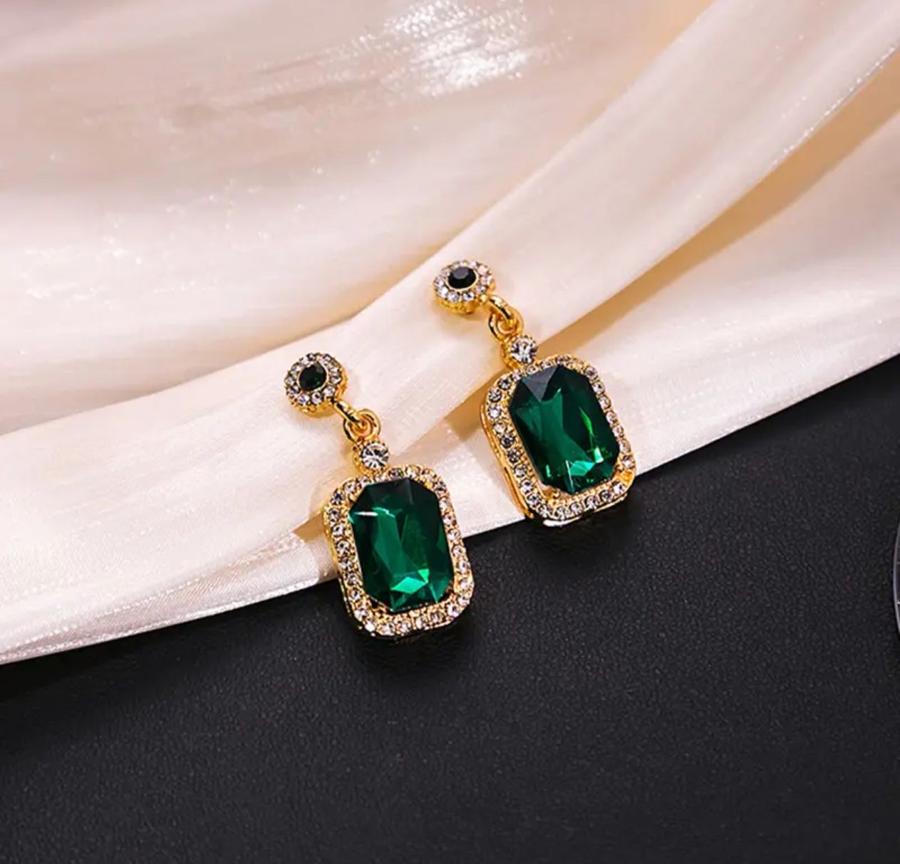 Pair of gold earrings featuring large faceted green rectangular stones surrounded by clear crystals