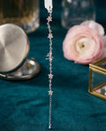 Silver bracelet with pink flower and green leaf crystals, featuring a dragonfly charm, displayed on teal fabric with a rose in background