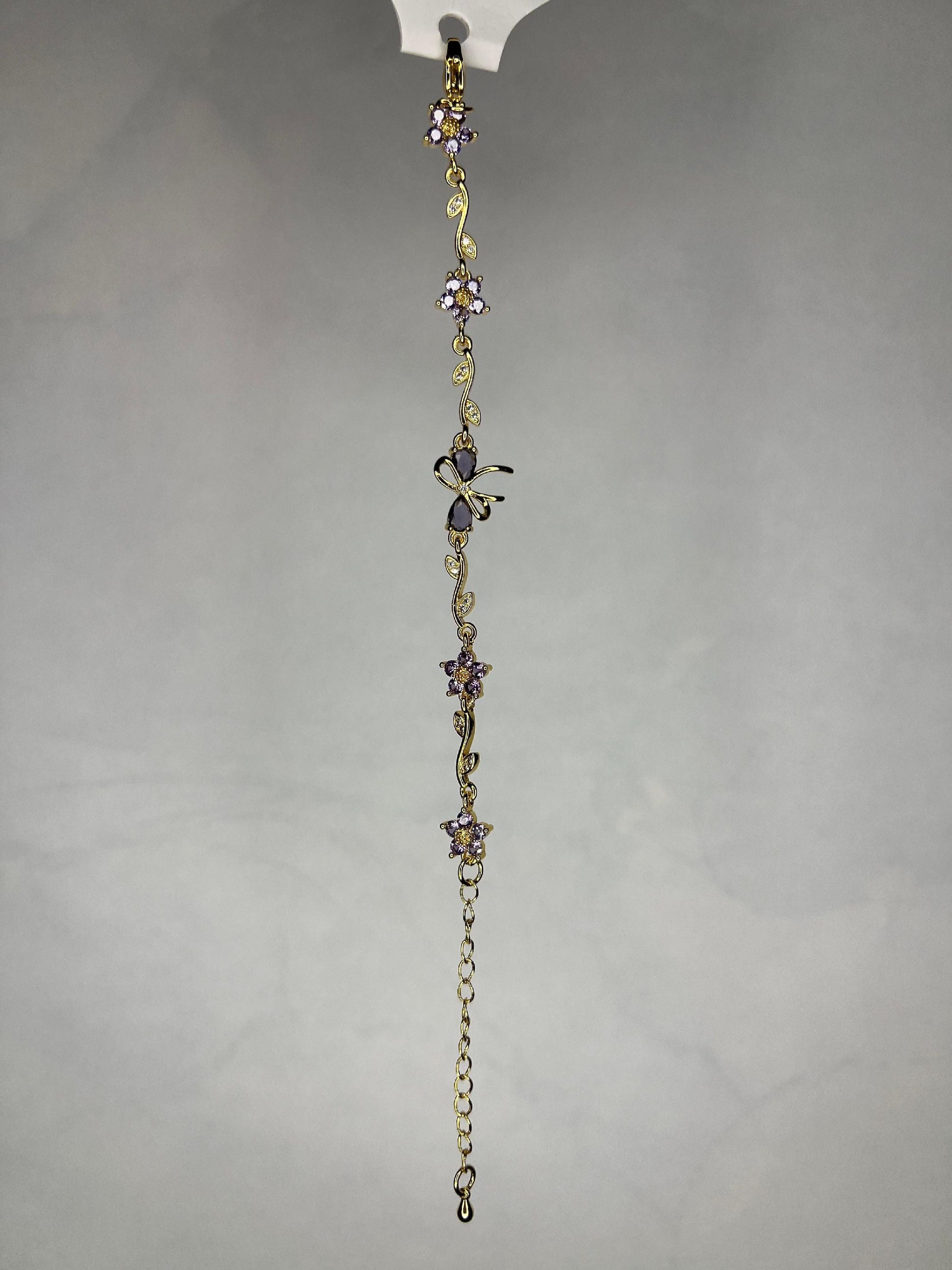 Close-up view of gold bracelet with floral and butterfly designs against a gray background