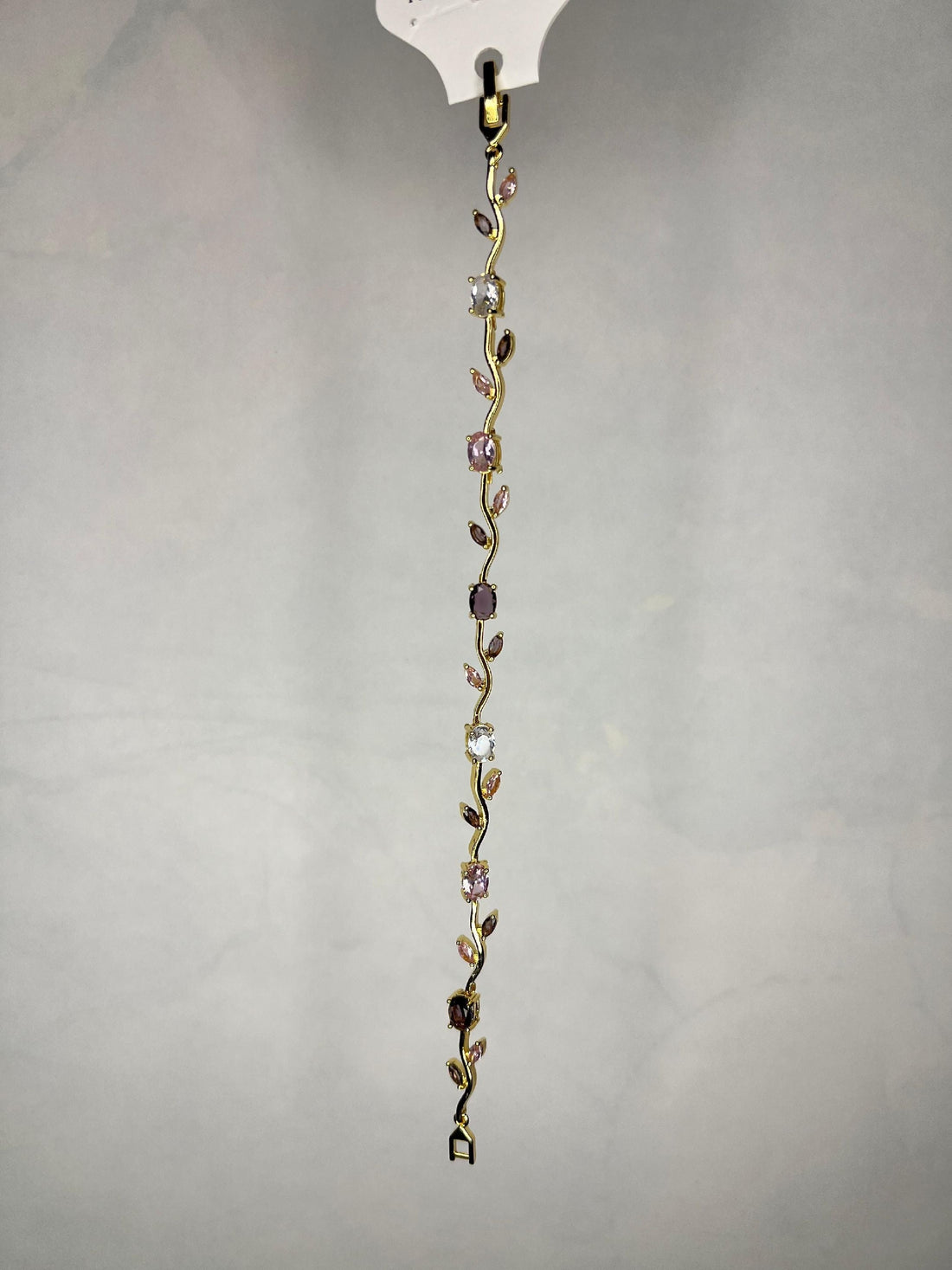 Gold-tone bracelet with pink and clear gemstones laid on black marble surface with rose petals