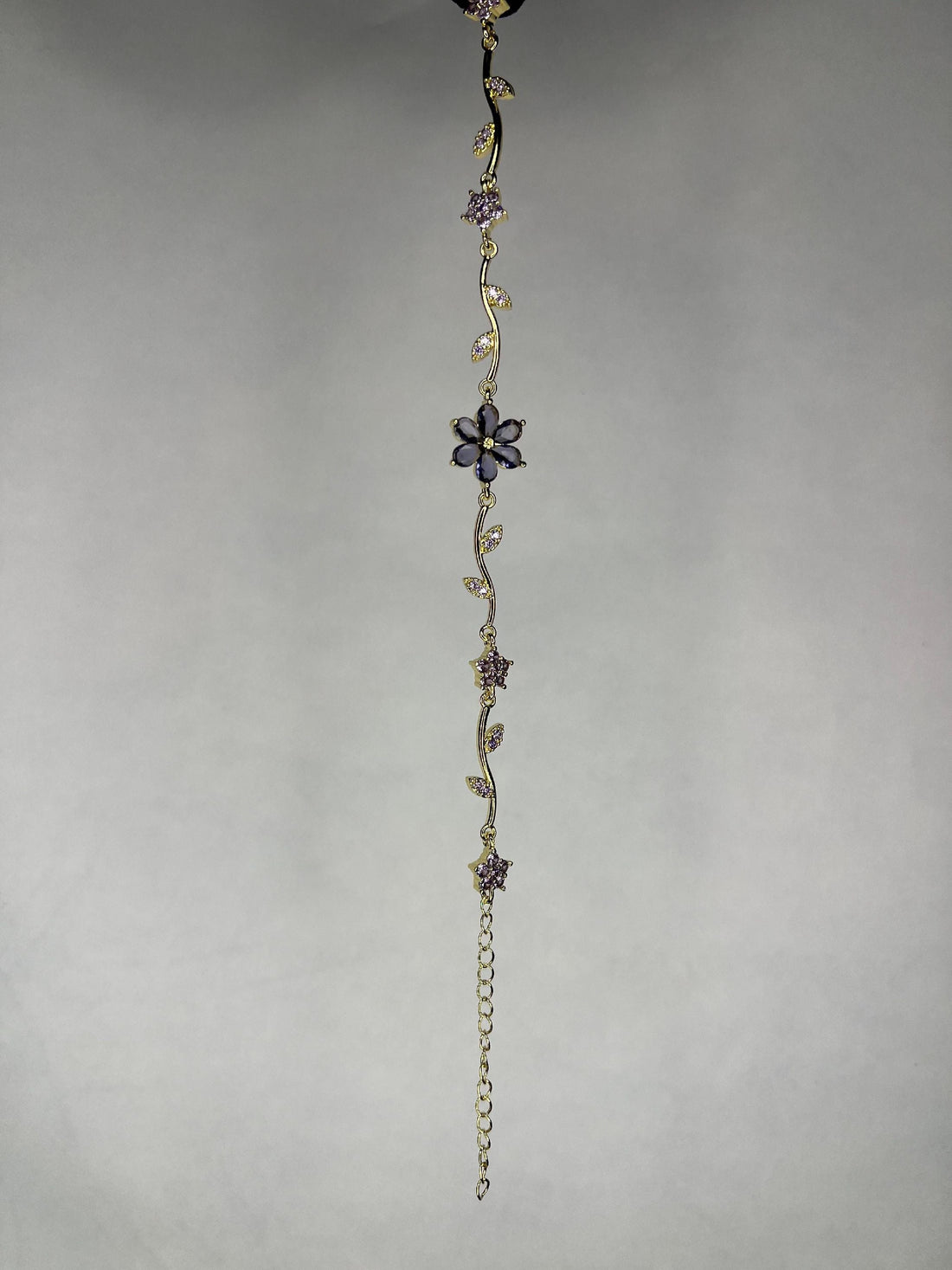 Gold-plated bracelet with amethyst flowers and leaves laid on black surface with amethyst stones