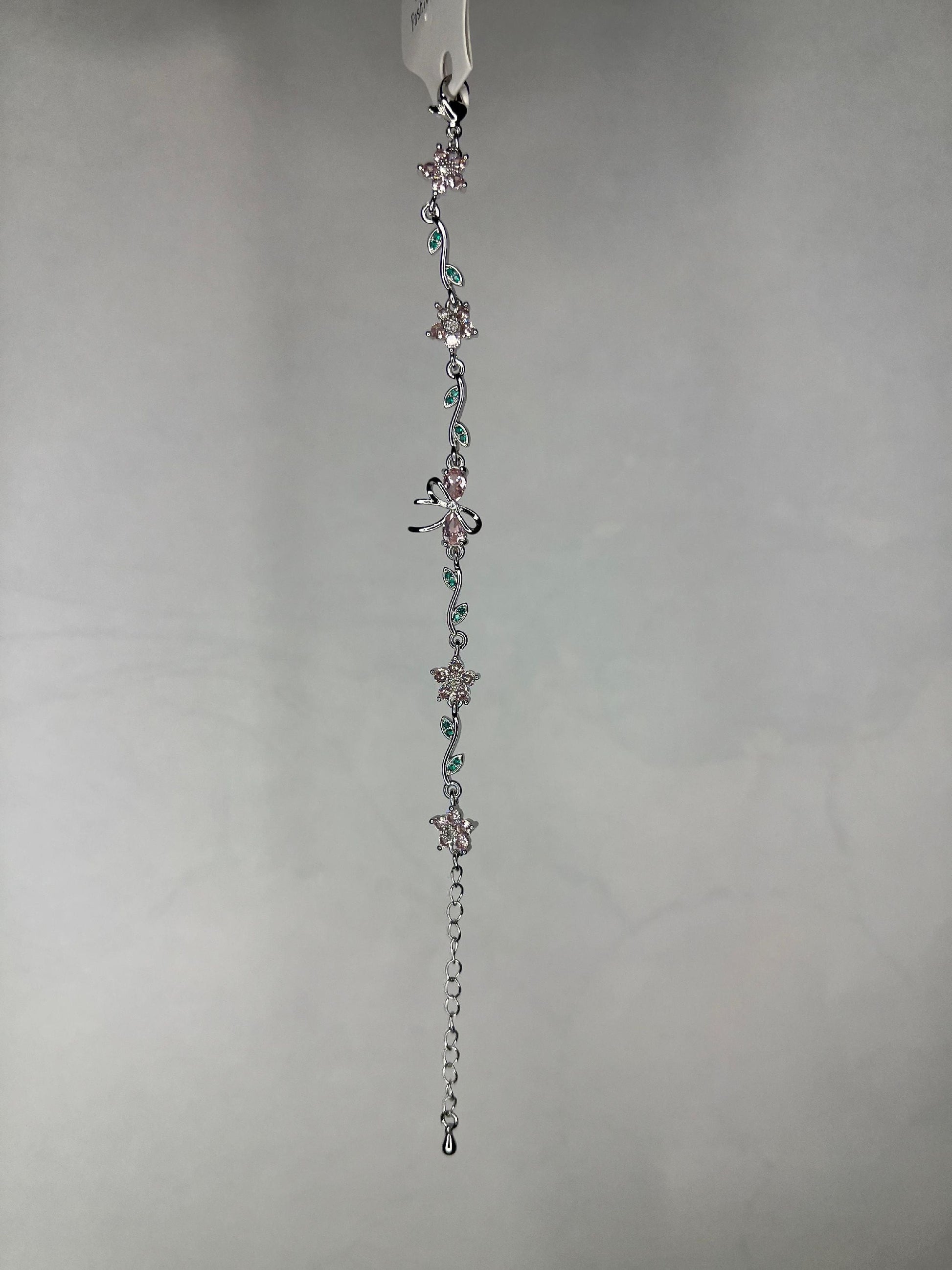 Close-up view of silver floral and dragonfly bracelet showing detailed pink and green crystal adornments on a plain background