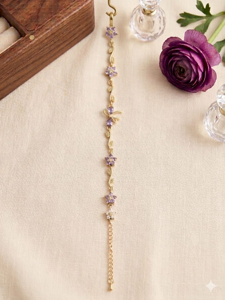 Gold floral amethyst bracelet displayed on cream fabric with purple flower and decorative glass bottles