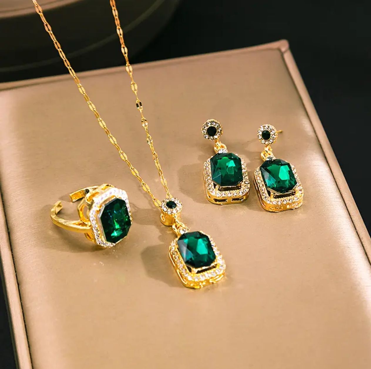 Complete jewelry set showing gold ring, necklace with pendant, and matching earrings with green stones and crystals