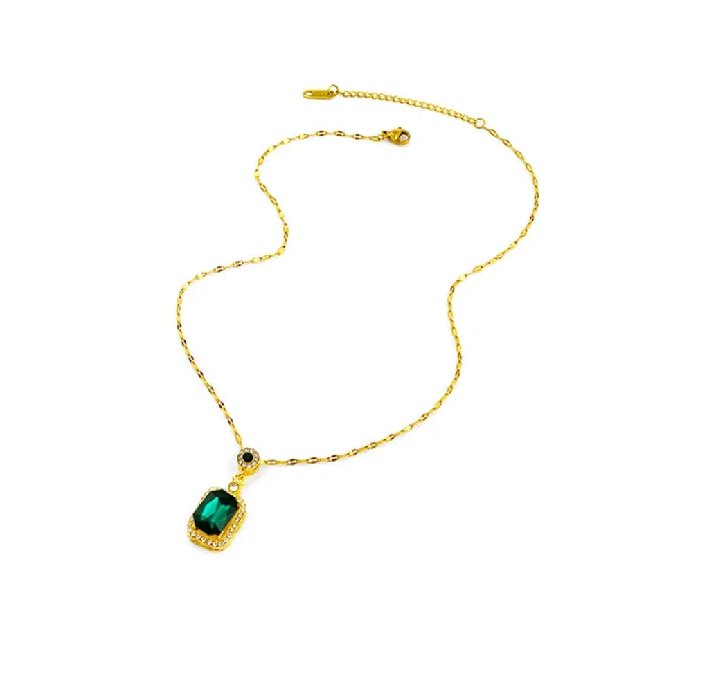 Gold chain necklace with rectangular green gemstone pendant bordered by clear crystals on a white background